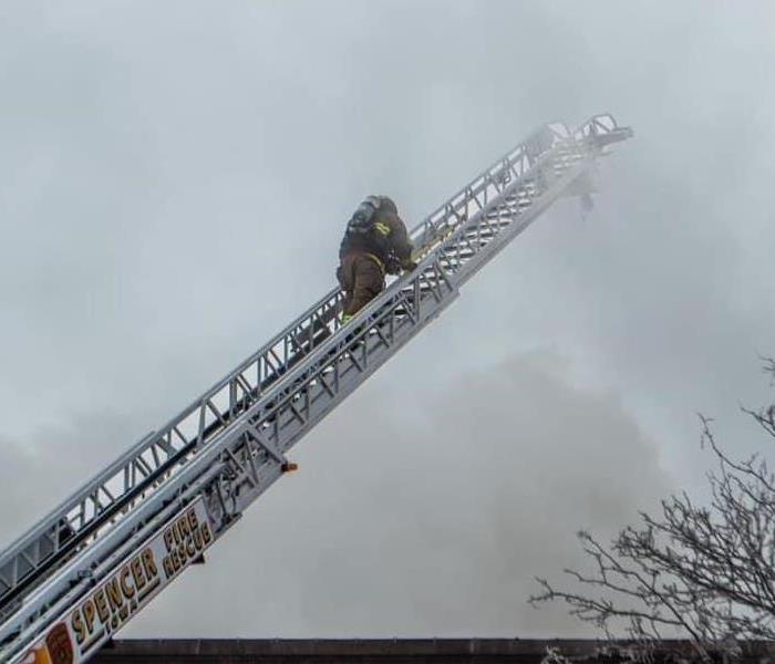 Firefighter on a ladder with heavy smoke around him. 